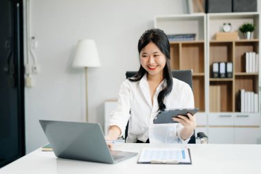 Ofiste çalışan genç iş kadını dizüstü bilgisayarı, tableti ve kâğıdı not alıyor.