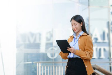 Zeki bir telefonu açık havada kullanırken gülümseyen kendine güvenen Asyalı iş kadını teknolojiyi, başarıyı ve modern profesyonel yaşam tarzını sembolize ediyor..