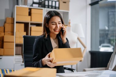 Girişimci Asyalı kadın çevrimiçi alışveriş için tablet ve dizüstü bilgisayarda paketler hazırlıyor ve çevrimiçi siparişleri kontrol ediyor.