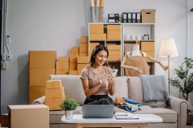 Girişimci Asyalı kadın çevrimiçi alışveriş için tablet ve dizüstü bilgisayarda paketler hazırlıyor ve çevrimiçi siparişleri kontrol ediyor.