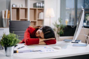 Asyalı kadın migren ağrısı çekiyor. Ofiste dizüstü bilgisayar ve tablet üzerinde çalışırken çok çalışan iş kadını finansör.