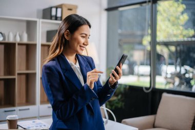 Kendine güvenen Asyalı iş uzmanı çekici, gülümseyen genç bir kadın yaratıcı ofiste elinde dijital tablet tutuyor.