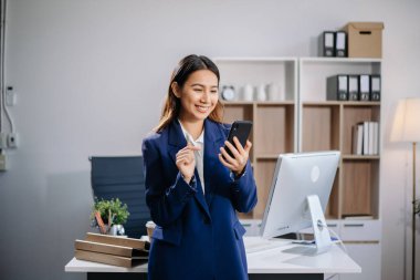 Kendine güvenen Asyalı iş uzmanı çekici, gülümseyen genç bir kadın yaratıcı ofiste elinde dijital tablet tutuyor.