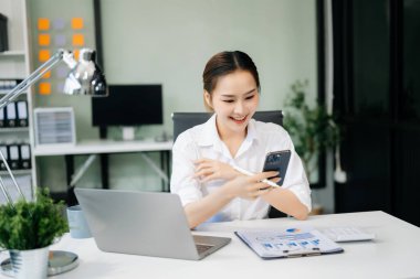 Confident Asian woman with a smile standing holding notepad and tablet at the modern office