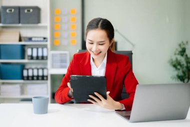 Confident Asian woman with a smile standing holding notepad and tablet at the modern office
