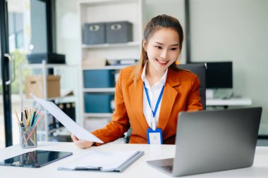 Çalışan not defteri, tablet ve dizüstü bilgisayarla çalışan genç Asyalı iş kadını akıllı telefon, tablet ve dizüstü bilgisayarla konuşuyor. Video arama vergisi, rapor, muhasebe 
