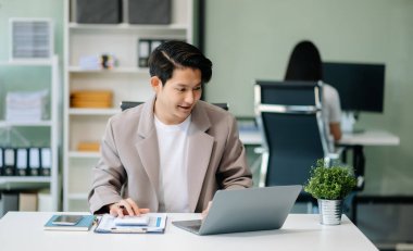 Modern ofiste elinde not defteri ve tabletle gülümseyen kendine güvenen Asyalı bir adam.