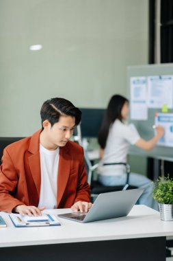 Modern ofiste elinde not defteri ve tabletle gülümseyen kendine güvenen Asyalı bir adam.