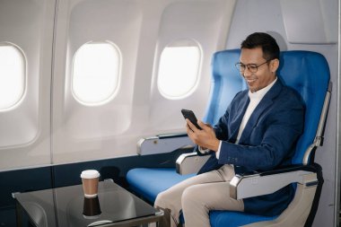 Genç Asyalı yönetici, dijital tablet, dizüstü bilgisayar ve akıllı telefondan birden fazla iş yaparak birinci sınıfta başarılı oluyor. Stil içinde seyahat et, zarafetle çalış.