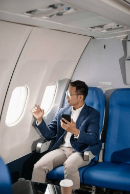 Genç Asyalı yönetici, dijital tablet, dizüstü bilgisayar ve akıllı telefondan birden fazla iş yaparak birinci sınıfta başarılı oluyor. Stil içinde seyahat et, zarafetle çalış.