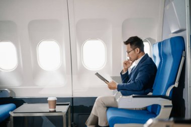 Genç Asyalı yönetici, dijital tablet, dizüstü bilgisayar ve akıllı telefondan birden fazla iş yaparak birinci sınıfta başarılı oluyor. Stil içinde seyahat et, zarafetle çalış.