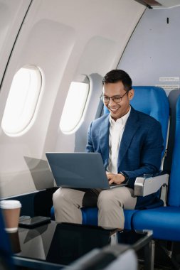 Genç Asyalı yönetici, dijital tablet, dizüstü bilgisayar ve akıllı telefondan birden fazla iş yaparak birinci sınıfta başarılı oluyor. Stil içinde seyahat et, zarafetle çalış.