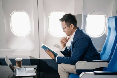 Genç Asyalı yönetici, dijital tablet, dizüstü bilgisayar ve akıllı telefondan birden fazla iş yaparak birinci sınıfta başarılı oluyor. Stil içinde seyahat et, zarafetle çalış.