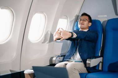 Hayal kırıklığına uğramış bir adamın uçakta kafası ellerindeyken çekilmiş fotoğrafı. Asyalı iş adamı uçakta oturmuş laptopta ve tablette çalışıyor. 