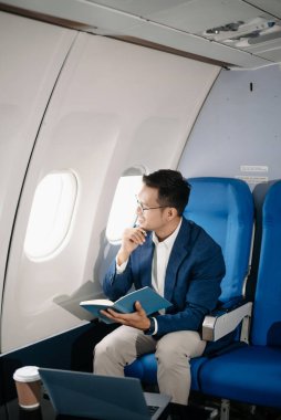 Genç Asyalı yönetici, dijital tablet, dizüstü bilgisayar ve akıllı telefondan birden fazla iş yaparak birinci sınıfta başarılı oluyor. Stil içinde seyahat et, zarafetle çalış.