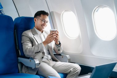 Genç Asyalı yönetici, dijital tablet, dizüstü bilgisayar ve akıllı telefondan birden fazla iş yaparak birinci sınıfta başarılı oluyor. Stil içinde seyahat et, zarafetle çalış.