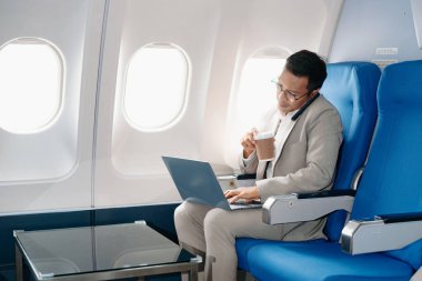 Genç Asyalı yönetici, dijital tablet, dizüstü bilgisayar ve akıllı telefondan birden fazla iş yaparak birinci sınıfta başarılı oluyor. Stil içinde seyahat et, zarafetle çalış.