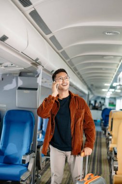 Çekici Asyalı erkek uçak yolcusu dizüstü bilgisayar ve tabletle kablosuz bağlantıyı kullanarak rahat koltukta oturuyor. Stil içinde seyahat et, zarafetle çalış.