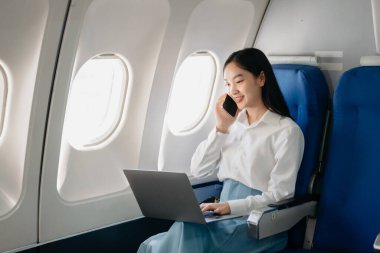 Genç Asyalı yönetici, dijital tablet, dizüstü bilgisayar ve akıllı telefondan birden fazla iş yaparak birinci sınıfta başarılı oluyor. Stil içinde seyahat et, zarafetle çalış.