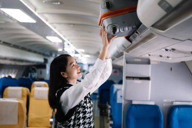 Çekici Asyalı kadın uçak yolcusu dizüstü bilgisayar ve tabletle kablosuz bağlantı kullanarak rahat koltukta oturuyor. Stil ve iş seyahatleri. 