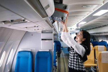 Çekici Asyalı kadın uçak yolcusu dizüstü bilgisayar ve tabletle kablosuz bağlantı kullanarak rahat koltukta oturuyor. Stil ve iş seyahatleri. 