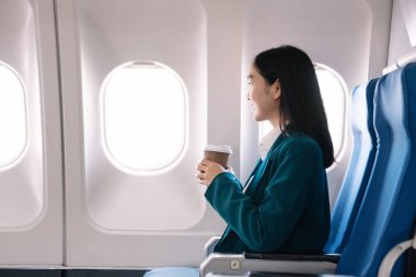 Çekici Asyalı kadın uçak yolcusu dizüstü bilgisayar ve tabletle kablosuz bağlantı kullanarak rahat koltukta oturuyor. Stil ve iş seyahatleri. 