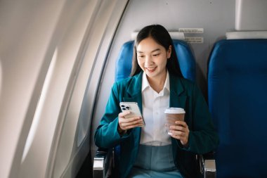 Çekici Asyalı kadın uçak yolcusu dizüstü bilgisayar ve tabletle kablosuz bağlantı kullanarak rahat koltukta oturuyor. Stil ve iş seyahatleri. 