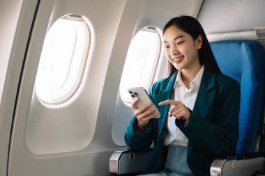 Çekici Asyalı kadın uçak yolcusu dizüstü bilgisayar ve tabletle kablosuz bağlantı kullanarak rahat koltukta oturuyor. Stil ve iş seyahatleri. 