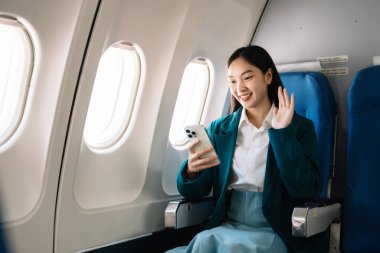 Çekici Asyalı kadın uçak yolcusu dizüstü bilgisayar ve tabletle kablosuz bağlantı kullanarak rahat koltukta oturuyor. Stil ve iş seyahatleri. 