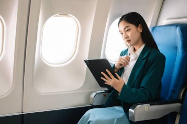 Çekici Asyalı kadın uçak yolcusu dizüstü bilgisayar ve tabletle kablosuz bağlantı kullanarak rahat koltukta oturuyor. Stil ve iş seyahatleri. 