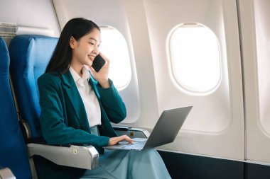Çekici Asyalı kadın uçak yolcusu dizüstü bilgisayar ve tabletle kablosuz bağlantı kullanarak rahat koltukta oturuyor. Stil ve iş seyahatleri. 