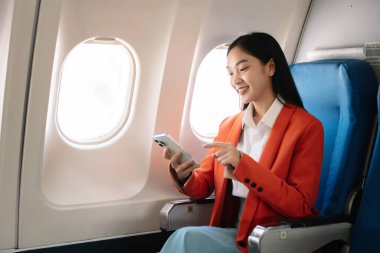 Çekici Asyalı kadın uçak yolcusu dizüstü bilgisayar ve tabletle kablosuz bağlantı kullanarak rahat koltukta oturuyor. Stil ve iş seyahatleri. 