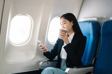 Çekici Asyalı kadın uçak yolcusu dizüstü bilgisayar ve tabletle kablosuz bağlantı kullanarak rahat koltukta oturuyor. Stil ve iş seyahatleri. 