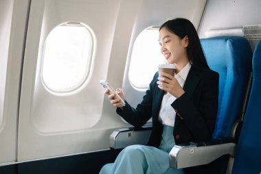 Çekici Asyalı kadın uçak yolcusu dizüstü bilgisayar ve tabletle kablosuz bağlantı kullanarak rahat koltukta oturuyor. Stil ve iş seyahatleri. 