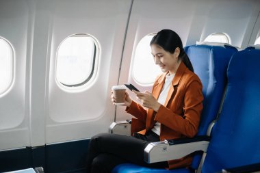 Başarılı bir Asyalı iş kadını portresi ya da resmi takım elbiseli bir girişimci, birinci sınıfta telefon ve bilgisayar laptopuyla oturuyor. Stil ve iş seyahatleri. 
