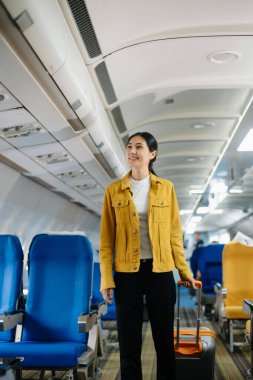 Çekici Asyalı kadın uçak yolcusu dizüstü bilgisayar ve tabletle kablosuz bağlantı kullanarak rahat koltukta oturuyor. Stil içinde seyahat et, zarafetle çalış..