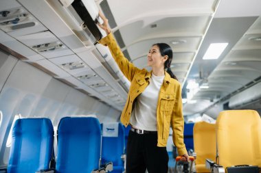 Çekici Asyalı kadın uçak yolcusu dizüstü bilgisayar ve tabletle kablosuz bağlantı kullanarak rahat koltukta oturuyor. Stil içinde seyahat et, zarafetle çalış..