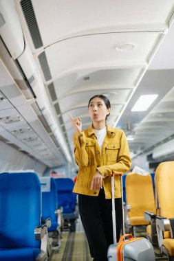 Çekici Asyalı kadın uçak yolcusu dizüstü bilgisayar ve tabletle kablosuz bağlantı kullanarak rahat koltukta oturuyor. Stil içinde seyahat et, zarafetle çalış..