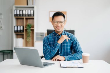 Young handsome man typing on tablet and laptop while sitting at the working table modern office