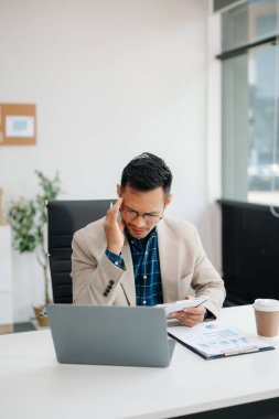 Genç yakışıklı adam çalışma masasında modern ofiste otururken tablet ve dizüstü bilgisayarda yazıyor.