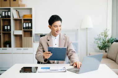 Genç Asyalı adamın çalıştığı yerde dizüstü bilgisayar ve tablet kullanması. İşine odaklan..