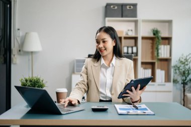 Kendine güvenen iş uzmanı, gülümseyen, dizüstü bilgisayarda yazan ve dijital tableti yaratıcı ofiste tutan çekici genç bir kadın..