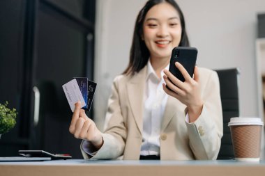 Asyalı kadın cep telefonuyla online alışveriş yapıyor, çok kanallı, masada oturuyor.