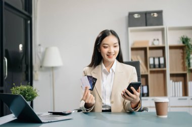 Asian Woman using smart phone for mobile payments online shopping, omni channel, sitting on table