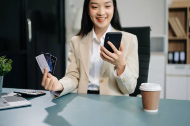 Asian Woman using smart phone for mobile payments online shopping, omni channel, sitting on table