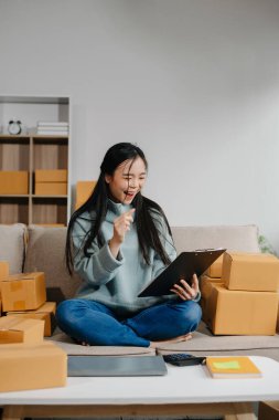 woman using smartphone or tablet taking receive and checking online purchase shopping order to preparing pack product box. Startup small business SME