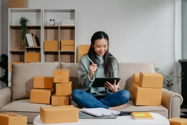 woman using smartphone or tablet taking receive and checking online purchase shopping order to preparing pack product box. Startup small business SME