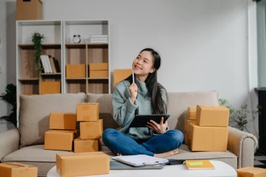 woman using smartphone or tablet taking receive and checking online purchase shopping order to preparing pack product box. Startup small business SME