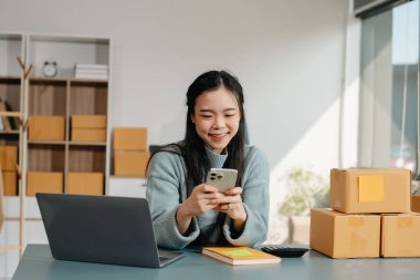Successful fashion designer. Attractive woman with smile while standing in workshop. Beautiful owner woman working and holds tablet, laptop and smartphone in studio.