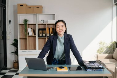 Çalışan not defteri, tablet ve dizüstü bilgisayarla çalışan genç Asyalı iş kadını akıllı telefon, tablet ve dizüstü bilgisayarla konuşuyor video arama vergisi, rapor, muhasebe 